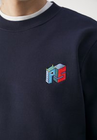 Sweatshirt bleu marine avec un col rond, arborant un logo géométrique brodé en rouge, bleu et vert sur la poitrine. Texture douce.