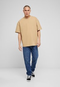 Camiseta corta beige de gran tamaño con hombros caídos, combinada con vaqueros rectos azules y zapatillas negras con acentos blancos.