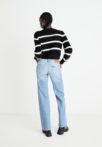 Black and white striped knit sweater paired with light blue high-waisted wide-leg jeans. Notable Lee tag on waistband and chunky black ankle boots.