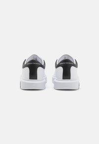 Sneaker bianco e nero con tomaia liscia in materiale sintetico e pannello posteriore a contrasto. Presenta una suola bianca spessa e un dettaglio del tallone con il marchio.
