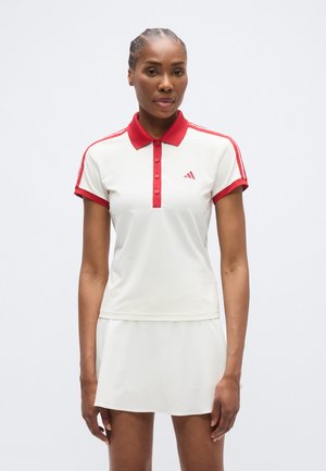 Polo bianca con colletto e dettagli rossi, con tre bottoni, abbinata a una gonna bianca coordinata. Design semplice, tessuto sportivo.