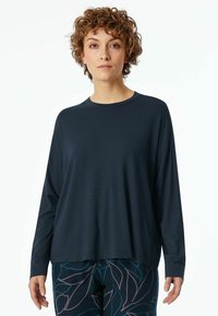 Navy long-sleeve top in a lightweight fabric with a crew neckline and relaxed fit. Paired with patterned pants featuring a leaf design.