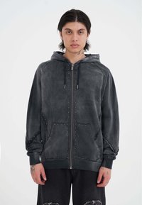 Sudadera con capucha de ante gris y cierre de cremallera, con acentos de tachuelas, bolsillos frontales y capucha con cordón. Presenta un corte relajado y mangas largas.