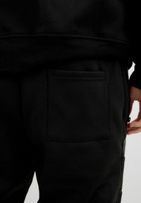 Pantalones jogger negros con un acabado texturizado, que cuentan con un bolsillo trasero y un bolsillo lateral con cremallera. Fabricados con un material ligero y transpirable.