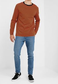 Långärmad tröja i röd och svart randig design, rund halsringning, matchad med blå jeans och svarta sneakers. Avslappnad passform.
