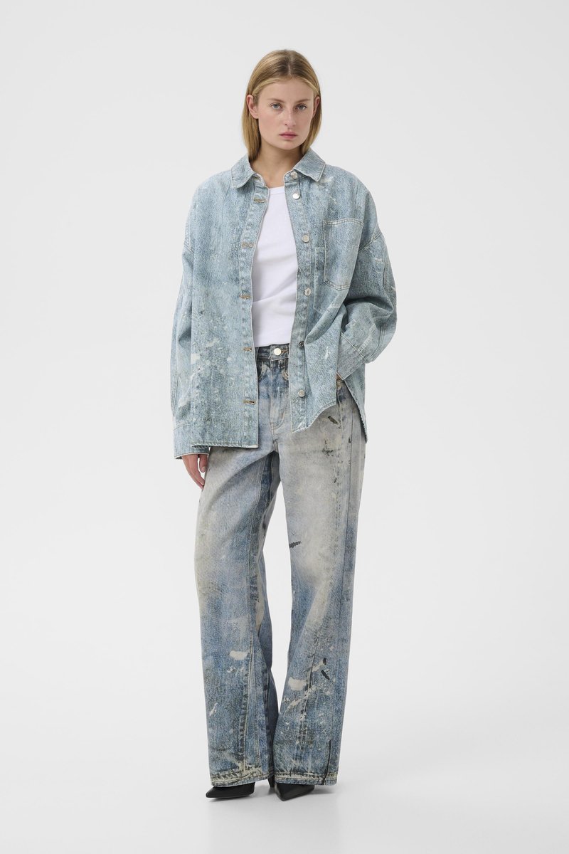 Chemise en denim bleu clair à la coupe décontractée, avec de grandes poches et des boutons. Associée à un jean bleu clair taille haute à jambes larges, avec des détails usés.