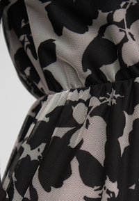 Sort og hvidt blomstermeshstof med samlet elastiksyning, der skaber tekstur og volumen.