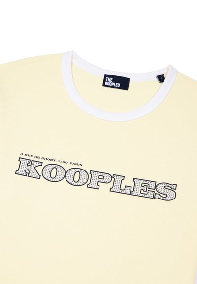 Pale yellow t-shirt with white round collar and "KOOPLES" text in bold patterned font with Paris address above.