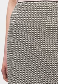 Gros plan d'une jupe en maille texturée noire et blanche portée par une personne debout, la main gauche détendue le long du corps.