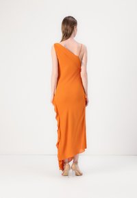 Orange, enaxlig klänning med draperad design, asymmetrisk fåll och mjuk textur. Bärs med nude-höga klackar, som har en sidofluffdetalj.