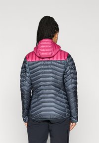 Puffatakki tummansinisin ja vaaleanpunaisin värein. Varustettu hupulla, tikatulla pinnalla ja muotoilultaan kapealla. Heijastavat yksityiskohdat parantavat näkyvyyttä.