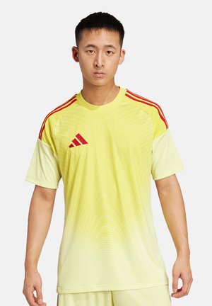 Geel sportshirt met een gradient ontwerp en subtiele golvende lijnen. Bevat rode schouderstrepen en een Adidas-logo. Korte mouwen, ronde hals.