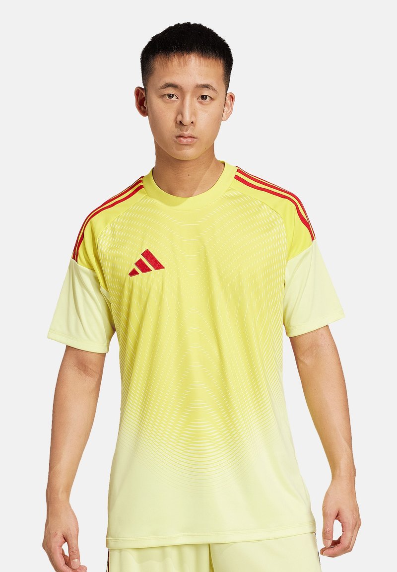 Gelbes Sporttrikot mit einem verlaufenden Design und subtilen Wellenlinien. Verfügt über rote Schulterstreifen und ein Adidas-Logo. Kurze Ärmel, Rundhalsausschnitt.