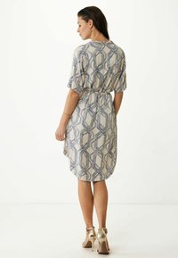 Vestido de patrón geométrico con mangas cortas, cintura ajustada y dobladillo a la altura de la rodilla; los colores incluyen crema y azul marino. Llevado con tacones dorados.