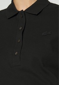 Polo shirt nera realizzata in tessuto texturizzato, con colletto classico, patta dei bottoni e un logo ricamato nero sul petto.