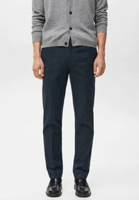Donkerblauwe wollen broek met een strak model, met een gladde textuur en subtiel patroon, gecombineerd met een grijze vest en zwarte schoenen.
