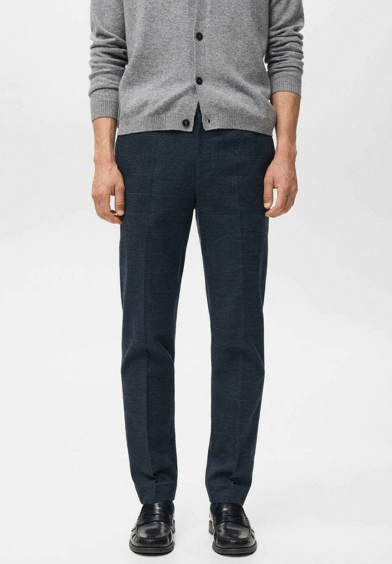 Donkerblauwe wollen broek met een strak model, met een gladde textuur en subtiel patroon, gecombineerd met een grijze vest en zwarte schoenen.