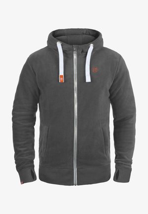 Felpa grigia in pile con lacci bianchi, chiusura con zip e tasche laterali. Presenta un logo sul petto e polsini e orlo a coste.