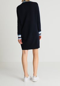 Robe en maille navy à manches longues, avec des poignets côtelés en bleu clair et des rayures blanches, d'une coupe décontractée, assortie à des baskets blanches.