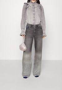 Szara koszula dżinsowa z falbankowymi rękawami, zapięciem na guziki oraz szerokimi spodniami dżinsowymi w kolorze szarym. Zawiera małą metaliczną torebkę oraz niebieskie obuwie.