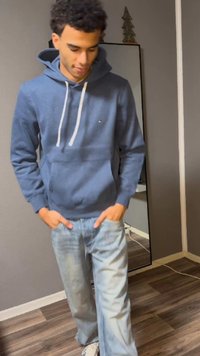 Blå hoodie med ficka framtill, dragsko i huvan och vita detaljer. Kombinerad med ljusblå, lätt slitna jeans. Trägolv i bakgrunden.