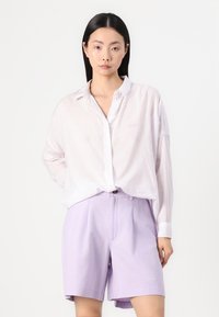 Svetlý pruhovaný košeľový dres v pastelovej ružovej a bielej farbe, doplnený fialovými šortkami. Košeľa má voľný strih a jemné vyšívané detaily.