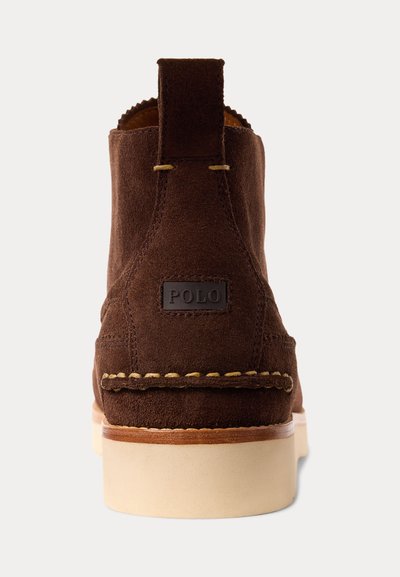 Bruine suède enkellaars met crème zool, zichtbare stiksels, trekkus aan de achterkant en een "POLO" label op de hiel.