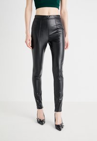 Leggings neri in pelle sintetica con vita alta, design aderente e dettagli di cucitura. Abbinati a tacchi neri a punta.