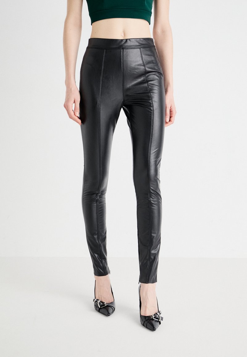 Leggings neri in pelle sintetica con vita alta, design aderente e dettagli di cucitura. Abbinati a tacchi neri a punta.