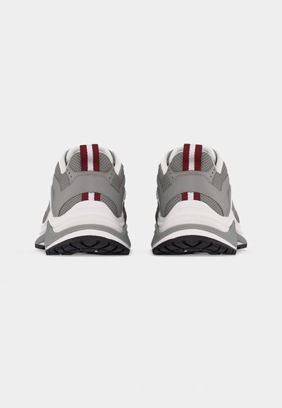 Ζευγάρι γκρι αθλητικά παπούτσια με λευκές μεσαίες σόλες και κόκκινες κάθετες ρίγες στην πίσω ετικέτα, ορατά από πίσω σε λευκό φόντο.