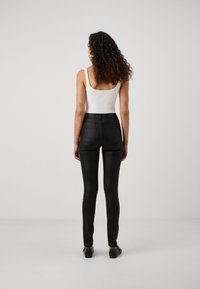 Svarta tights med slim fit, slät yta och elastisk midja, kombinerat med en vit linne, sett bakifrån.