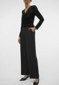 Haut en dentelle noire avec un design froncé, col en V et manches longues, associé à un pantalon noir à rayures verticales taille haute et des ballerines noires pointues.
