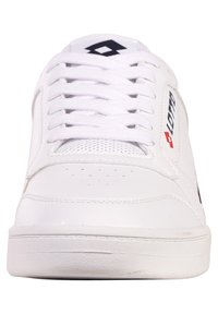 Białe sportowe buty z gładką skórzaną cholewką, perforowanym palcem, płaskimi sznurówkami i teksturowaną gumową podeszwą. Zawierają akcenty z logo w kolorze czerwonym i niebieskim.