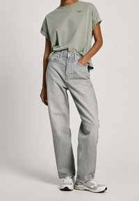 Ljust grön oversized t-shirt med uppvikta ärmar, grå högmidjade jeans och vita sneakers med grå detaljer. Avslappnat outfit med minimal branding.