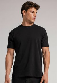 Schwarzes Kurzarm-T-Shirt aus glattem Baumwollstoff. Verfügt über einen Rundhalsausschnitt und eine lockere Passform. Verstärkte Nähte am Saum.