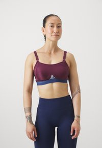 Reggiseno sportivo in un profondo bordeaux con spalline regolabili e un band blu in contrasto. Tessuto morbido, coppe preformate e una texture liscia.