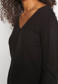 Maglione nero a scollo a V con lavorazione a maglia texturizzata, maniche lunghe e vestibilità rilassata. Il tessuto appare morbido e caldo.
