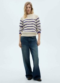 Maglione lavorato a maglia color crema con strisce viola, abbinato a jeans larghi blu scuro. Entrambi hanno una vestibilità morbida e un tessuto strutturato.