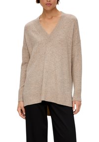 Beige v-hals trui met ribbelstructuur en zoom, met lange mouwen en een losse pasvorm, gecombineerd met zwarte broek.
