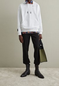 White hoodie with drawstrings and front pocket, layered over a multicolored floral collared shirt. Black tapered pants and black ankle boots.