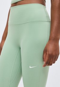 Κοντινό πλάνο προσώπου που φοράει ανοιχτοπράσινο κολάν Nike με ψηλή μέση και ορατές ραφές σε λείο ύφασμα.