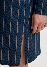 Indumento blu a fantasia con un motivo a logo ripetuto, strisce verticali marroni e bianche, con uno spacco laterale e una texture liscia.