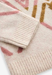 Manche et bas d'un pull en maille douce couleur beige clair avec des poignets en côtes et des motifs abstraits roses et bruns sur le tissu.