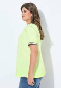 T-shirt a maniche corte, dalla vestibilità ampia, di un vivace giallo neon con polsini accentati in grigio. Tessuto testurizzato e un piccolo logo etichetta all'orlo.