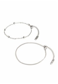 Las pulseras de metal plateado presentan cadenas delicadas con pequeños acentos esféricos, una de ellas con un cierre ajustable y un detalle de etiqueta.