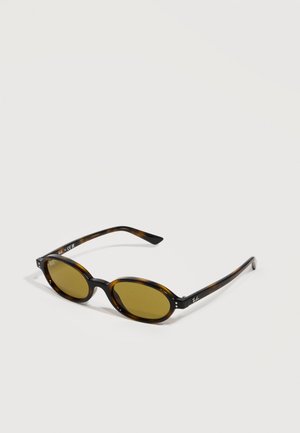 Ovale Sonnenbrille mit Schildpatt-Muster, braunen Gläsern und dünnen Bügeln, auf einer weißen Oberfläche liegend.