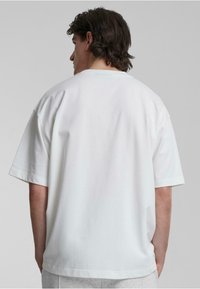 Hvit oversized t-skjorte laget av bomull, med korte ermer og rund hals. Glatt tekstur med et enkelt, ensfarget design.