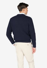 Granatowy sweter dzianinowy z okrągłym kołnierzem, ściągaczami na mankietach i u dołu. Noszony z jasnymi, dopasowanymi spodniami z bocznymi kieszeniami.
