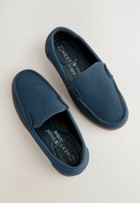 Ballerines bleu marine en tissu doux, avec une surface lisse, un bout arrondi et une semelle en caoutchouc brun contrastant. Étiquette indiquant "Ortholite Ultra."