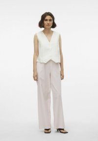 Witte linnen mouwloze vest met een V-hals en knoopdetail, gecombineerd met lichtroze, wijde geruite broek. Platter sandalen maken de look af.